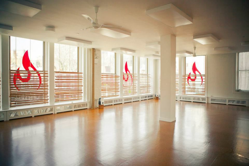 Empty Modo Yoga studio with tall windows, a wood floor and heaters on the ceiling