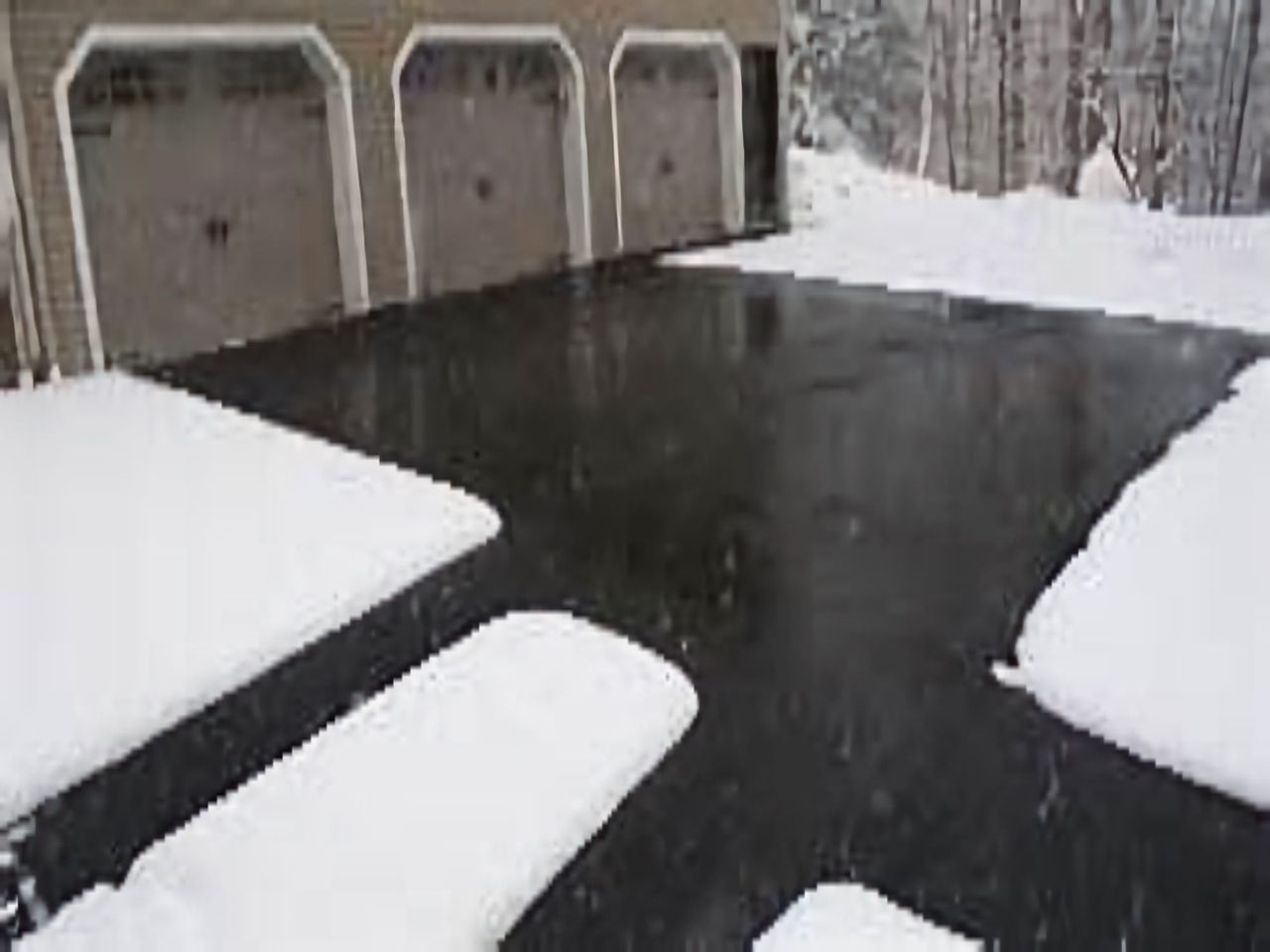Clear black asphalt driveway in front of a three-car garage, with snow on both sides